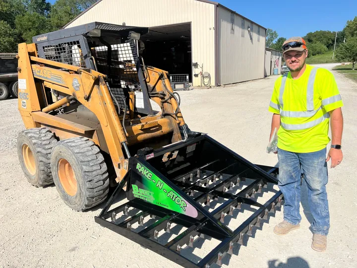 78-inch B-Built Rake-N-Ator on a Case skid steer, with a man in a safety vest beside it
