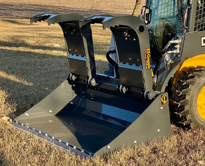 Solid bucket with dual grapples on a skid steer in a field